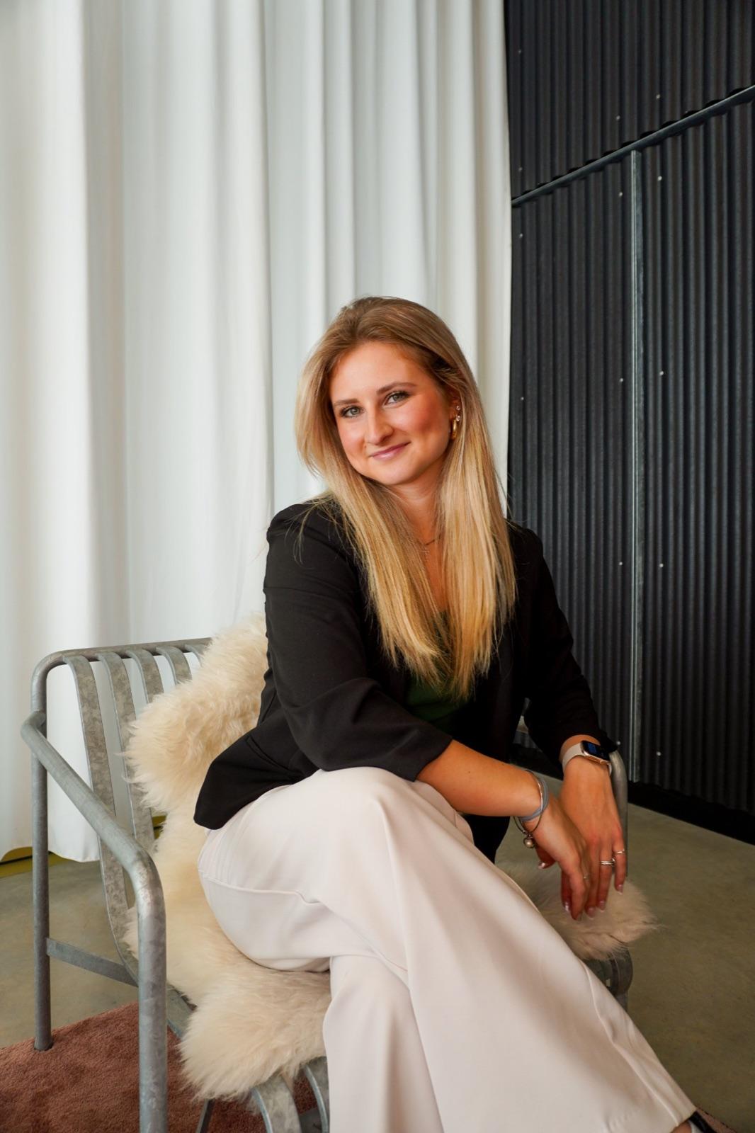 Abigail Rowland smiling, seated in a black blazer and cream trousers